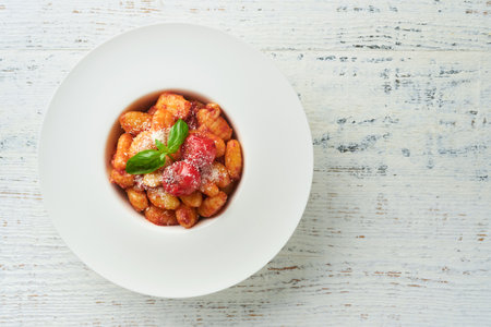 Potato gnocchi. Traditional homemade potato gnocchi with tomato sauce, basil and parmesan cheese on kitchen table on light gray kitchen table background. Traditional Italian food. top view.の写真素材