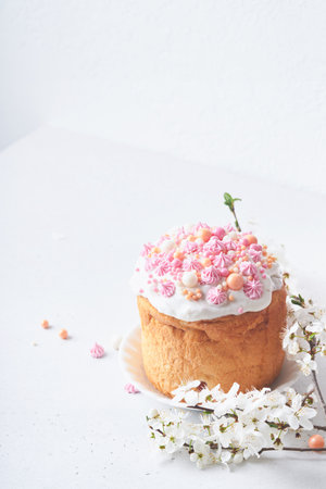 Traditional Easter sweet bread or cakes with white icing and sugar decor, colored eggs and cherry blossom tree branch over white table. Various Spring Easter cakes. Happy Easter day. selective focus.の写真素材