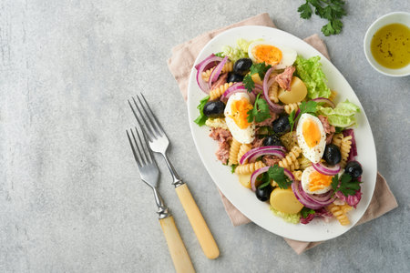 Tuna salad with pasta, eggs, potatoes, olives, red onions and sauce in white plate on old light gray concrete table background. Nicoise salad. french cuisine. top view. flat lay.の写真素材