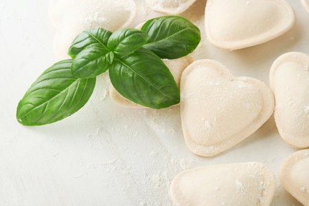 Italian ravioli pasta in heart shape. Tasty raw ravioli with flour and basil on white background. Food cooking ingredients background. Valentines or Mothers Day lunch ideas. Top view with copy space.の写真素材