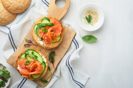 Open smoked salmon sandwiches with cream cheese, cucumber, sesame seeds, microgreens, spinach, and peas leaves on light old wooden background. Healthy breakfast food. Delicious snack. Top view.の写真素材