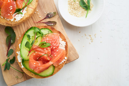 Open smoked salmon sandwiches with cream cheese, cucumber, sesame seeds, microgreens, spinach, and peas leaves on light old wooden background. Healthy breakfast food. Delicious snack. Top view.の写真素材