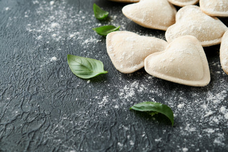Italian ravioli pasta in heart shape. Tasty raw ravioli with flour and basil on dark background. Food cooking ingredients background. Valentines or Mothers Day lunch ideas. Top view with copy space.の写真素材