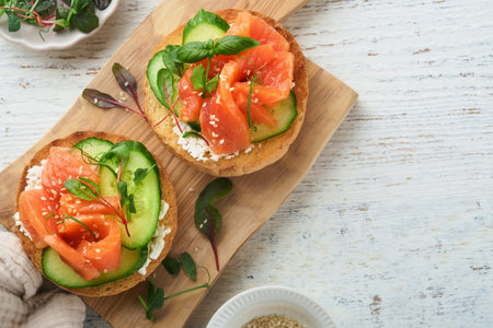 Open smoked salmon sandwiches with cream cheese, cucumber, sesame seeds, microgreens, spinach, and peas leaves on light old wooden background. Healthy breakfast food. Delicious snack. Top view.の写真素材