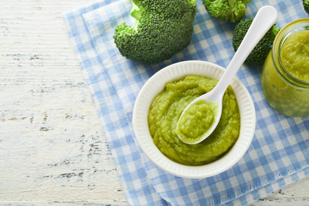 Green broccoli baby food in white bowl and jar on table. Green baby food. Child first feeding concept. Baby Natural Food. Production and menu of baby food. Selective focus.の写真素材