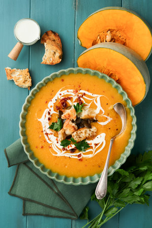 Pumpkin and carrot cream soup with herbs, seasonings and seeds in bowl on dark wooden background in rustic style. Thanksgiving traditional autumn pumpkin cream soup. Top view.の写真素材