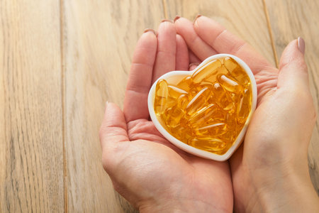 Female or doctor holds in hand capsules with Vitamin D, E or Omega 3,6,9 fatty acids in heart shape bowl. Food supplement oil filled fish oil. Natural supplements for healthy good life concept. Bannerの写真素材