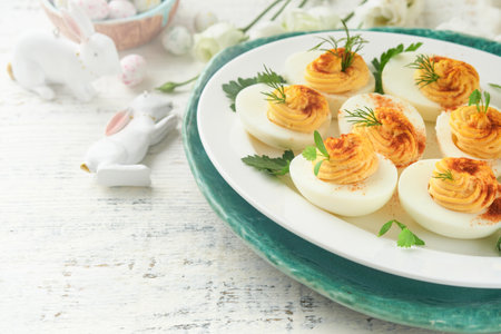 Easter stuffed eggs. Traditional Easter brunch or dinner with stuffed eggs with paprika, carrot cake bars and chocolate nest cakes with glazed eggs. Easter meal dishes with holday decorations Top viewの写真素材