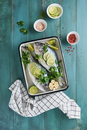 Raw fresh. Fresh raw dorado with lemon, lime, parsley and salt on old wooden blue background ready...