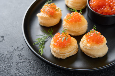 Salmon red caviar toast. Christmas canape or toast with red caviar on black plate on dark background. Idea for xmas snack. Gourmet food. Texture of caviar. Seafood.の写真素材