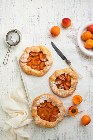 Apricot galette. Homemade three small apricot pie with fresh apricot served for summer tea party on old wooden light table background. Traditional family recipe. Top view with copy space.の写真素材