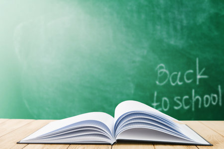 Open black cover book or notebook against the background of a school green board with sunbeams. Back to school training concept. Empty background.の写真素材