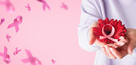 Pink Breast Cancer Awareness Ribbon. Female hands holding red gerbera with flying pink ribbon on pink backgrounds. Breast cancer awareness and October Pink day, world cancer day. Top view. Mock up.の写真素材