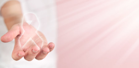 Pink Breast Cancer Awareness Ribbon. Man hand holds flying luminous pink ribbon icon in sun rays on pink background.October Pink day, world cancer day. Top view. Mock up.の写真素材