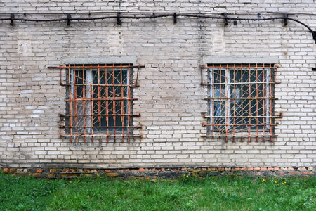 Two windows with metal bars on the old brick wall of an abandoned building.の写真素材