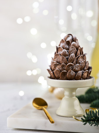 Festive brownie cake shaped Christmas tree pine cones with powdered sugar in the atmosphere of Christmas table with bokeh garland on light background. Christmas and New Year baking idea recipe.の写真素材