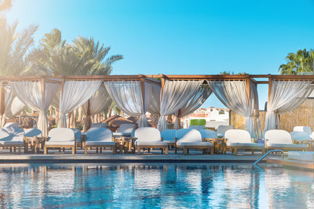 Beach chairs canopy. Luxurious hotel with private pool and beach chairs canopy under umbrellas palm trees and sun loungers for relaxation. Concept summer travel and vacation background.の写真素材