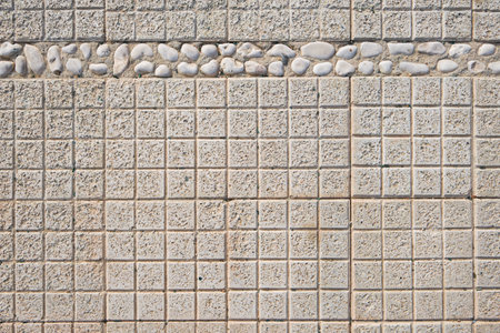 Square tiles and round pebbles concrete wall covered with gray cement surface textured. Gray old wall with shabby damaged plaster or cement and brick background of vintage dirty exfoliating plaster.の写真素材