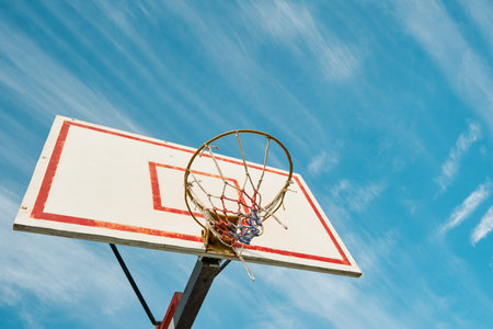 Old Basketball hoop on blue sky with clouds and sun glare on sunny day. Concept of success, scoring points and winning, healthy lifestyle, sports. Copy space.の写真素材