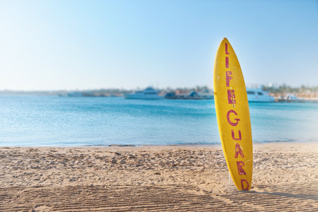 Lifebuoy circle and surfboard for rescue. Scenic view of red and white lifebuoy on post on seaside beach. Scenery landscape of sea ocean shore on sunny day. Water rescue concept.の写真素材
