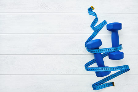Fitness or healthy lifestyle concept. Blue dumbbells wrapped with blue measuring tape on white wooden background with copy space. Minimal sports accessories idea. Top view with copy spaceの写真素材