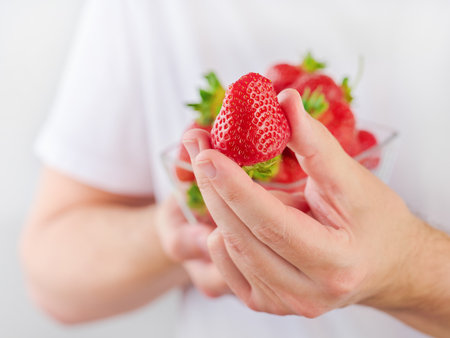 Fresh strawberries in plate in male hands for treat or show. Young man in white T shirt holds strawberry in his hand for treat. Element for design. Healthy eating lifestyle concept.の写真素材