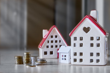 Three white toy houses with red roof and stack of money coins on wooden background. Family home, purchase and rent of apartments concept. Copy space.の写真素材