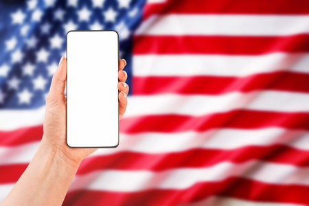 Female hand holding smartphone with blank screen for text or product background USA flag. Labor day, 4th of July, memorial day holiday concept. Design element.の写真素材