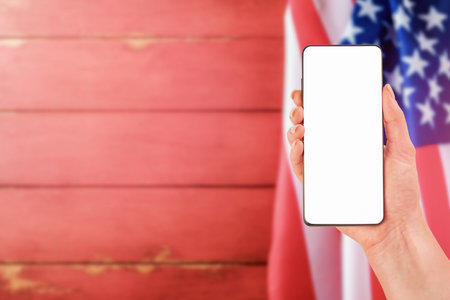 Female hand holding smartphone with blank screen for text or product background USA flag. Labor day, 4th of July, memorial day holiday concept. Design element.の写真素材