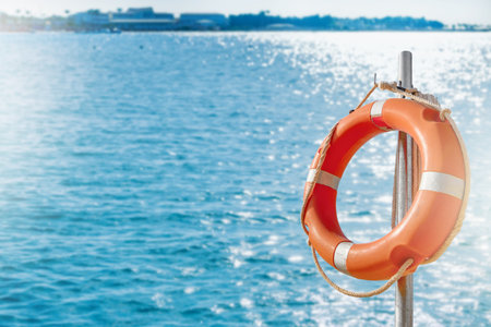 Lifebuy circle. Scenic view of red and white lifebuoy on post on seaside beach. Scenery landscape of sea ocean shore on sunny day. Water rescue concept.の写真素材