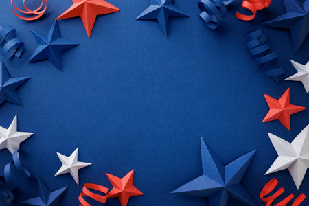 Festive arrangement of red, white and blue paper stars and curled ribbons on dark blue background. Patriotic border with empty space for text, suitable for Independence, Fourth of July, Memorial, Veterans or Flag day, national celebrations, invitations and greeting cards.