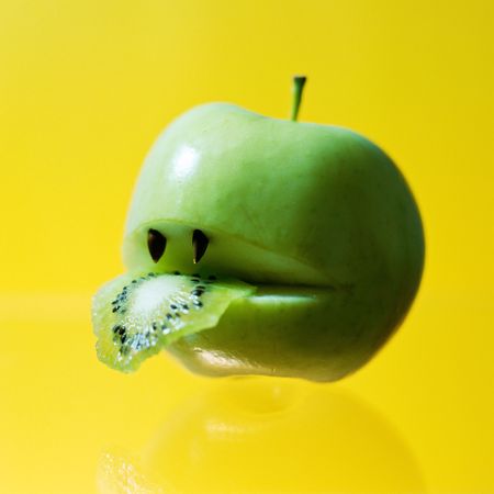 Hungry apple eating slice of kiwiの写真素材