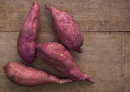 Four whole pink sweet potatoes on a wooden areaの写真素材