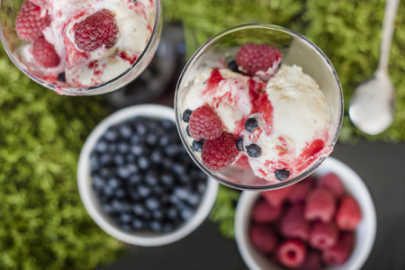 Ice cream with fruits raspberries, blueberries and with raspberries syrup, stay in glass on moss, one spoon is in backgroundの写真素材