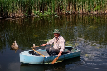 an elderly fisherman on a small iron boat in a small riverの写真素材