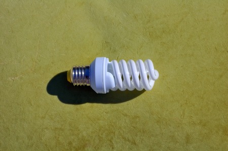 A shiny spiral fluorescent light bulb with highlights and a silvertone base, on a green backgroundの写真素材