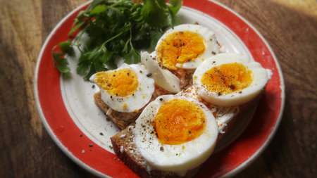 A healthy breakfast of boiled eggs on toast, seasoned with pepper and fresh herbs.の写真素材