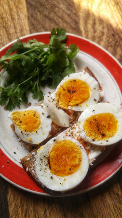 A healthy breakfast of boiled eggs on toast, seasoned with pepper and fresh herbs.の写真素材