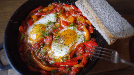 Hearty shakshuka with eggs, peppers, tomatoes, herbs, and breadの写真素材