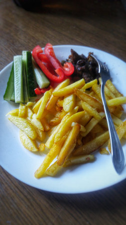 A plate of golden French fries, fresh vegetables, and meat, a complete meal.の写真素材