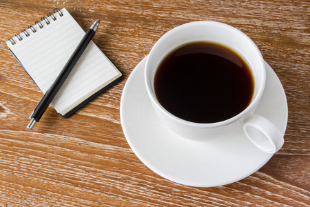 White cup of coffee on wooden table with notebookの写真素材
