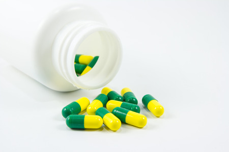 Green and yellow pills out of bottle on white backgroundの写真素材