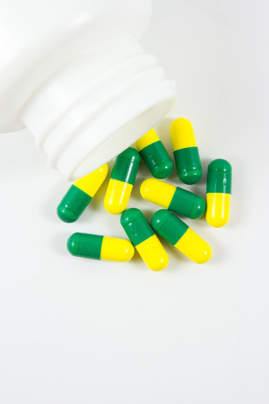 Green and yellow pills out of bottle on white background with copyspaceの写真素材