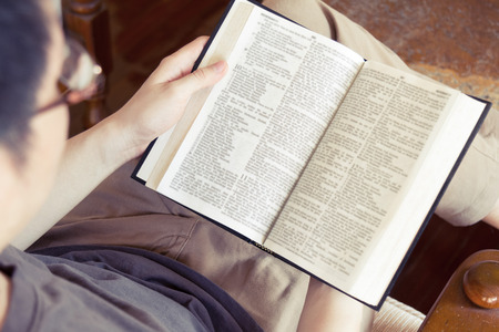 young man sitting on sofa and reading book, over shoulder viewの写真素材