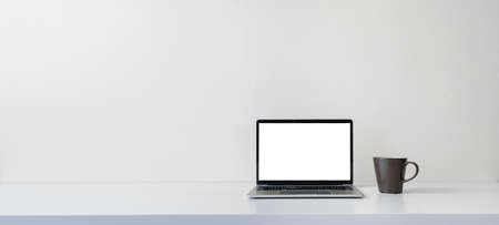 Modern contemporary workspace with blank screen laptop computer and coffee cup on office desk table on white wall background for copy space. Home office workplace concept.の写真素材
