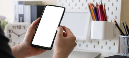 Male freelancer or business man hands using mobile phone with blank white screen for mock up at home office table. Work at home concept.の写真素材