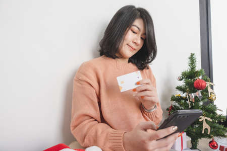 young asian woman sit on floor, using mobile phone, and holding credit card for christmas online shoppingの写真素材