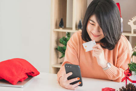 happy young asian woman using mobile phone and holding credit card for christmas online shoppingの写真素材