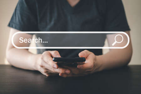 Man hand using mobile phone for searching and browsing internet information. Using search bar on website. Computer data technology, search engine optimization, and network concept.の写真素材