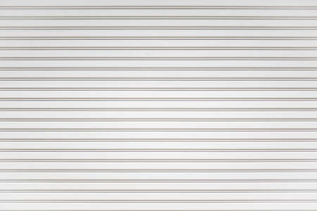 White metal roller shutter door background. Steel stripe horizontal lines of iron foldable metal sheet texture. Empty front warehouse garage door abstract pattern.の写真素材